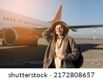 tourism, vacation and people concept - happy smiling young woman wearing hat with travel bag pack standing by the airplane and ready to departure.