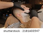 Barber Man is shaving client with a vintage straight razor in a barbershop. Shaving cream, foam. Classic shave by stainless steel straight edge razor