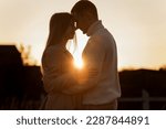 Small photo of Silhouette of loving couple couple at sunset is hugging and touching nose to nose outdoors at park. Young man and woman falling in love have romantic date on Valentine's day.