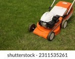 Small photo of Top view of modern orange-grey electric lawn mower cutting bright lush green grass. Gardening work tools. Rotary lawn mower machine on lawn. Professional lawn care service. Place for text.