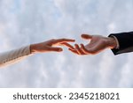 Hands of bride in white dress and groom in suit reaching each other, touching fingers on blue sky background. Helping hands for save and support people concept. Wedding day. Valentine day