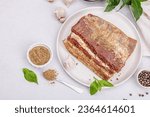 Small photo of Piece of salty high-fat meat cooked with spices. Salo, bacon, lard, silverside, gammon. Garlic, fresh bay leaves, spices. Light stone concrete background, top view