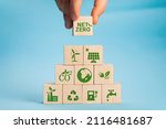 Net zero and carbon neutral concept. Net zero greenhouse gas emissions target. Climate neutral long term strategy. Hand put wooden cubes with green net zero icon and green icon on grey background.