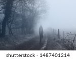 A ghostly woman walking along a country path on a spooky misty winters day. With a cold, blue edit.