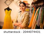 Portrait of Young happy indian woman, fashion designer tailor standing with crossed arms, measurement tape in garment workshop, seamstress, tailoring clothing on mannequin in  studio. skill india