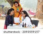 Small photo of Young Indian adult girl with her mother getting proscription medicine by female doctor at village outdoor at government camp, woman examine by medical person, Rural India healthcare.