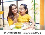 Small photo of Young Indian mother feed her little daughter noodles breakfast at table, Little girl child having food with her mom spoon feeding . selective focus