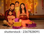 Small photo of Portrait of happy young Indian family in traditional dress with lots of gifts around sitting on floor celebrating diwali festival at home.
