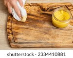 Small photo of Woman hands apply homemade beeswax wood treatment polish to restore natural wood cutting board. Beeswax, olive oil and essential oil, soft cloth and mixture in glass jar. Polishing wood.