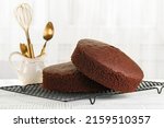 Just baked plain Chocolate sponge cake on the cooking iron grid, white table. Fluffy, moist and rich chiffon Cake, homemade. Cooking utensils.