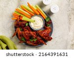 Small photo of Baked spicy BBQ Chicken Wings smothered in barbecue sauce. Serwed with White Sauce dip and celery and carrot sticks. Light background. Top view.