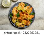 Small photo of Plate with Fried in a batter Zucchini Flowers stuffed with ricotta cheese and parsley. Raw and Roasted courgette or pumpkin flowers. Italian dish fiori di zucca in pastella. Stone background.