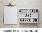 'Keep calm and carry on' words on a modern board, clipboard with blank sheet of paper on a white wooden background, top view. Overhead, from above, flat lay. 