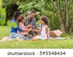 Cheerful family sitting on the grass during a picnic in a park, there is a basket with meal and toys for the kids