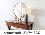 Round mirror hanging on light beige wall, Mid Century Wood Console Table in the interior of a modern room with a lamp.