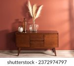 Mid-Century Modern Wooden Sideboard with Glass Vase Decoration Set with Pampas grass, Against a Salmon-Colored Wall in the Interior of a Living Room with Wooden Flooring.