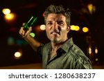 Small photo of young upset and aggressive drunk man in pub at night holding beer bottle threatening ready to fight as the violent thug troublemaker in every bar and alcohol addict furious guy