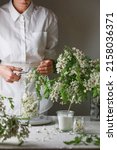 Small photo of Woman wearing in white dress put acacia flowers in a jar. Girl prepares acacia jam.