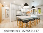 Small photo of Modern farmhouse kitchen interior with light wood floors white granite marble counters large dining table with eight chairs stainless appliances orange color accents and large windows with black trim