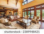 Spacious living room interior with exposed wooden beams ship like finishing wooden staircase with wrought iron hardware stone fireplace leather furniture overstuffed chairs view to dining and kitchen