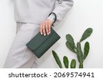 Small photo of green clutch in the hands of a woman in a light gray suit