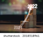 Small photo of Shining rise up arrow on wooden blocks chart steps with percentage icons from year 2021 to 2022 on wooden desk, business growth process, and economic improvement concept.