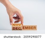 Small photo of Changing to the last month of the year. The hand is flipping wooden cube blocks for change words, months from November to December on the desk on white background, clean, modern, and minimal style.