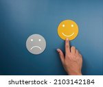 Small photo of Customer service evaluation, ratings, feedback, client experience, satisfaction survey concepts. Happy smile on yellow face chosen by customer's hand near sad face on blue background, minimal style.