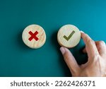 Small photo of Right and wrong. Close-up green check mark and red X mark icon on round wooden button, chosen green check mark by business's hand. Picking correct sign. Approving, voting or right decision concepts.