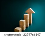 Big arrowhead wooden on increase cube blocks bar graph chart steps on dark blue background with copy space. Investment, income, trends, inflation, business growth, economic improvement concepts.