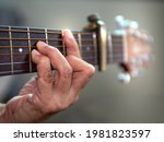 Small photo of Old woman musician hand holds the neck of classic wooden guitar play Bm chord. Senior female guitarist put fingers on fingerboard playing B Minor chord song. String musical instrument background.