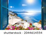 View from an open window with blue shutters of the Aegean sea, caldera, coastline and whitewashed town of Oia, Santorini, Greece.