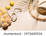 Summer flat lay on beige background. Straw hat and lemon fruits in eco friendly mesh shopping bag. Trendy palm shadow and sunlight, sun. Minimal summer travel fashion concept.