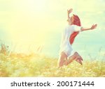 Beauty Girl Outdoors enjoying nature. Beautiful Teenage Model girl in white dress jumping on summer Field with blooming wild flowers, Sun Light. Free Happy Woman. Toned in warm colors