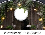Small photo of Blank minimal circular shop signboard mockup for design. Street hanging sign board for logo presentation with light garland amond the leaves. Metal cafe restaurant or bar badge black white round.
