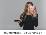 Small photo of Portrait of a sad girl with a smartphone in one hand and a smiling mask in the other hand, with which she covers her face, as a symbol of the inconsistency of the image of a person in social networks