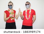 man and woman posing near white wall with glasses of champagne in hand. boy and girl wearing hawaiian flowers and face masks to protect from coronavirus. celebrating new year 2021 at home quarantine.