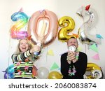 attractive man and young woman celebrating new year 2022 at home quarantine. boy holding alarm clocks. girl shooting confetti. big number balloons. silvester party. december 31. lockdown. january 1.