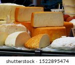 Small photo of various types of delicious large cut round soft cheese pieces in yellow and white color. open food market with cheese on display. rich food concept. deary food. food production and agriculture.