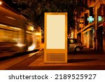 brightly lit advertising panel at tram stop on urban street. night scene. glass and metal structure. poster ad display. light box. banner and copy space. streetscape. mockup base. motion blurred tram