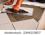Small photo of male worker's hands and metal trowel tool. spreading cement based underlayment on concrete floor base. laying large ceramic tile floor. work in progress. construction work process concept.