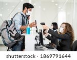 Male traveler shows phone to female officer at airline check in counter for issue airplane ticket boarding pass. Woman staff wear face mask to prevent from coronavirus pandemic. New normal lifestyle