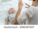 Small photo of Caucasian loving mom play with cute baby boy child on bed in bedroom. Happy family, attractive beautiful caring young mother ticklish on toddler son enjoying activity relationship in morning in house.