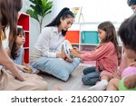 Caucasian beautiful young woman teacher teaching art to kids at school. Attractive Instructor master female explain and educate drawing and painting with student kindergarten pre school in classroom.