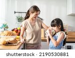 Small photo of Asian little cute kid holding a cup of milk and drinking with mother. Attractive mom teach and support young girl daughter take care of her body, sipping a milk after wake up for health care in house.