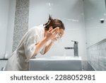 Asian beautiful woman washing her clean face with facial foam and water. Attractive female in bathrobe washing face for healthy beauty treatments and skin care then looking at the mirror in bathroom.