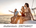 Small photo of Group of diverse friend sit on deck of yacht while yachting together. Attractive young men and women hanging out, celebrating holiday vacation trip while catamaran boat sailing during summer sunset.