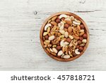 Wooden bowl with mixed nuts on white table from above. Healthy food and snack. Walnut, pistachios, almonds, hazelnuts and cashews.
