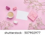 Morning cup of coffee, cake macaron, gift or present box and flower on pink table from above. Beautiful breakfast. Flat lay style.