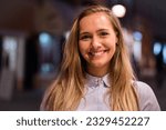 Close up portrait of a beautiful woman with long blonde hair outdoors in the city center in the evening.